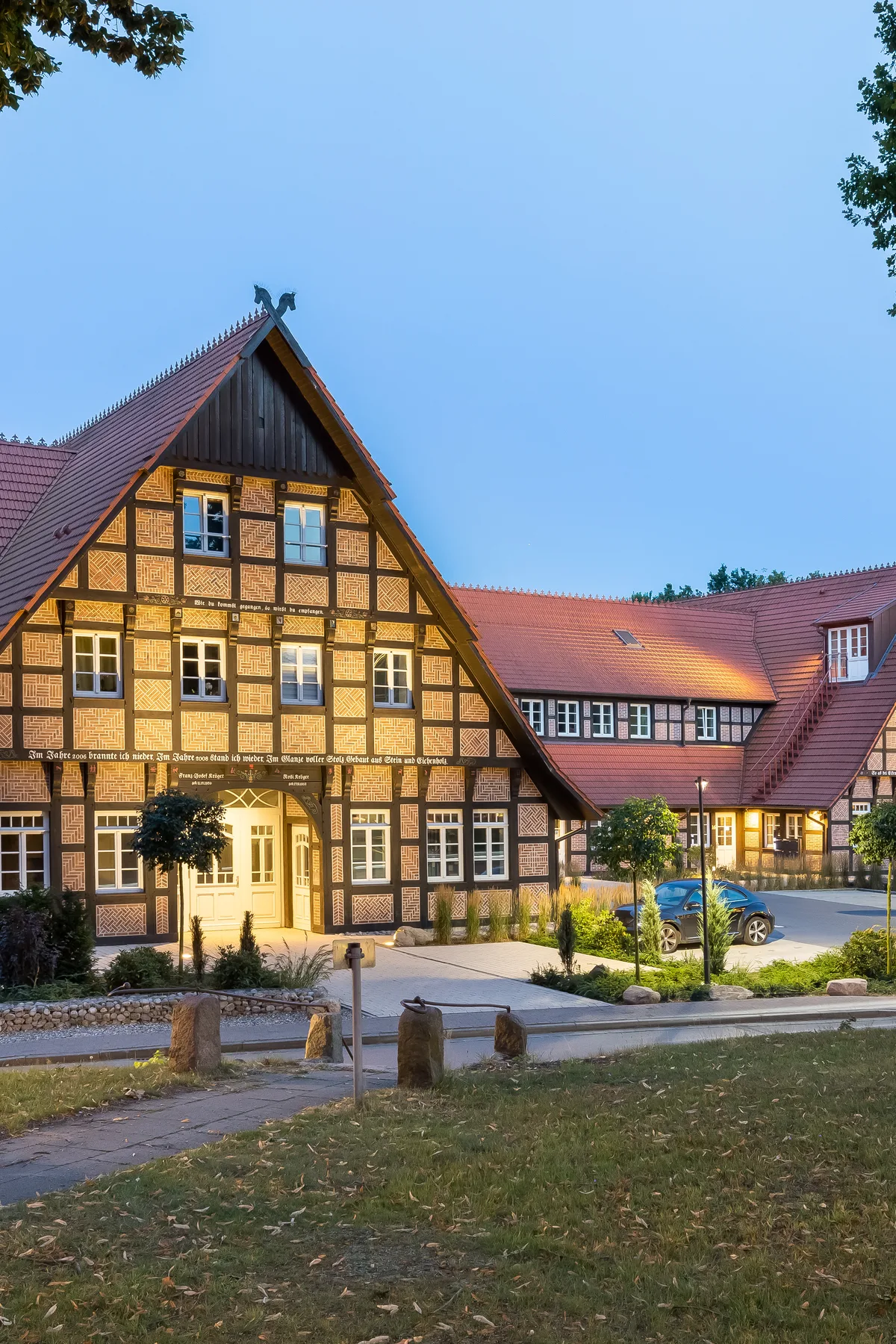 Fertiges Fachwerk-Ensemble zur blauen Stunde mit beleuchteten Fenstern, eingerahmt von zwei alten Bäumen