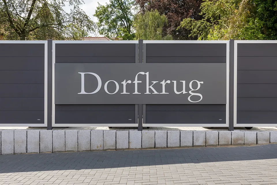 Schriftzug Dorfkrug auf einer dunklen Einfassung an der Zufahrt
