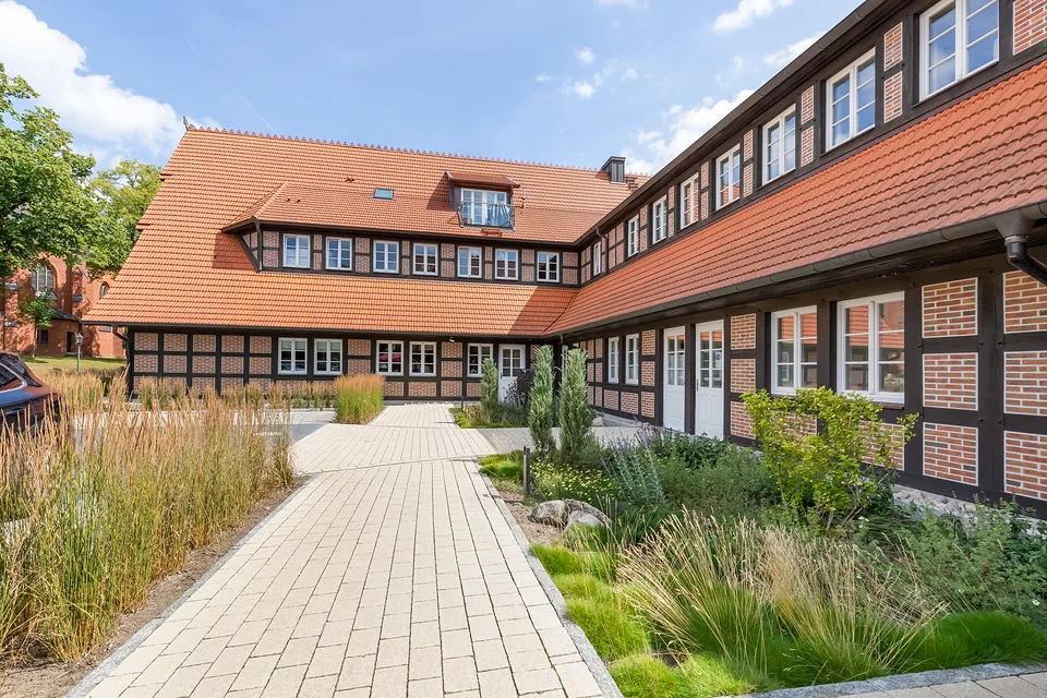 Gepflasterter Weg mit Gräsern entlang eines Fachwerk-Seitenflügels