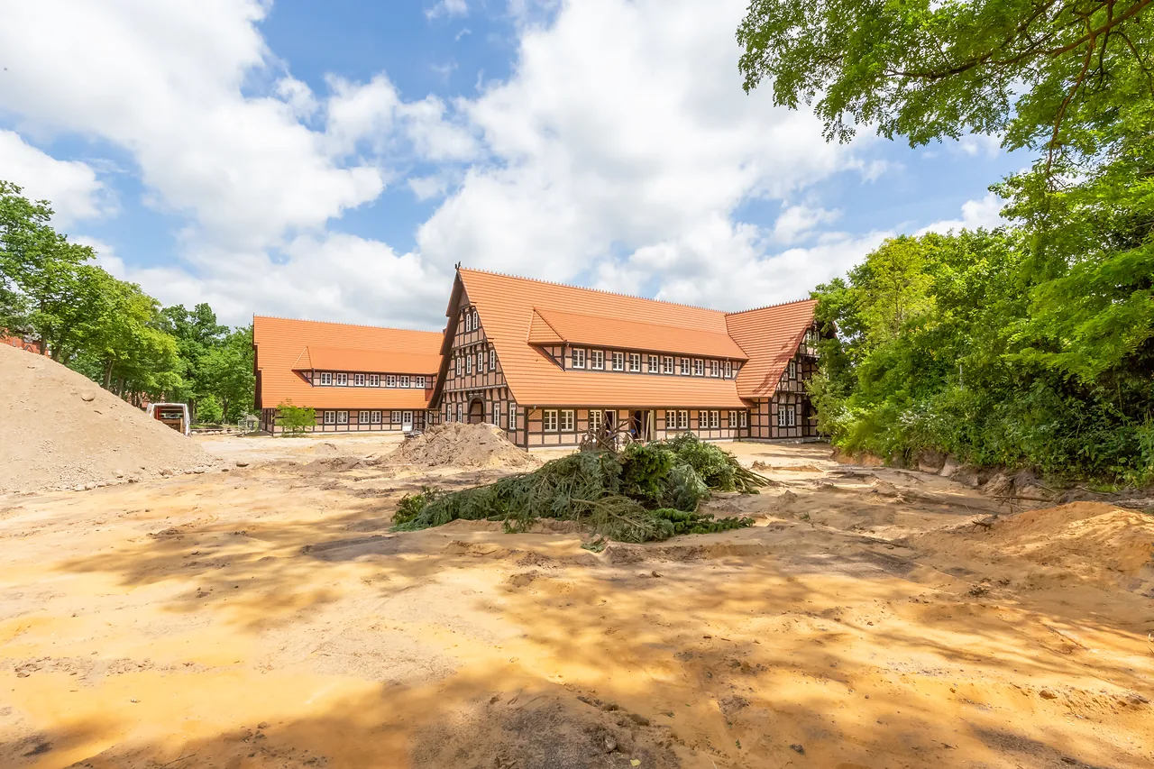 Rohbau: Fachwerkhaus mit Seitenflügeln, davor Baustellenfläche und Erdhaufen