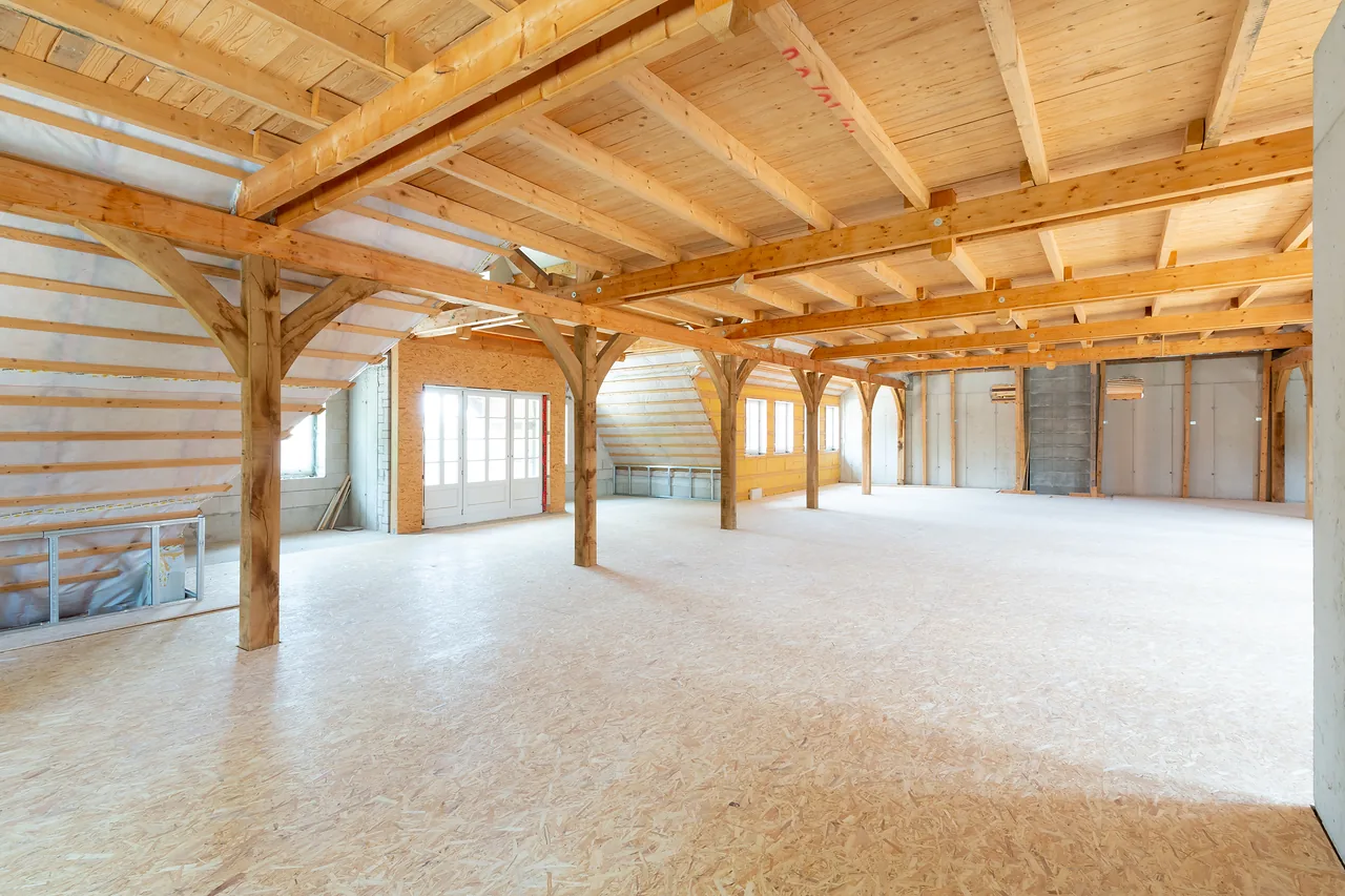 Rohbau: offenes Dachgeschoss mit Holzstützen, Kopfbändern und Rohboden
