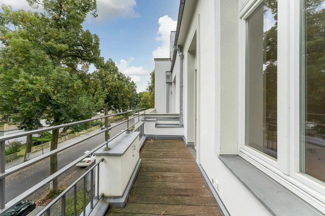Nachher: Balkon mit Holzdielen und Geländer, Bäume und blauer Himmel mit Wolken