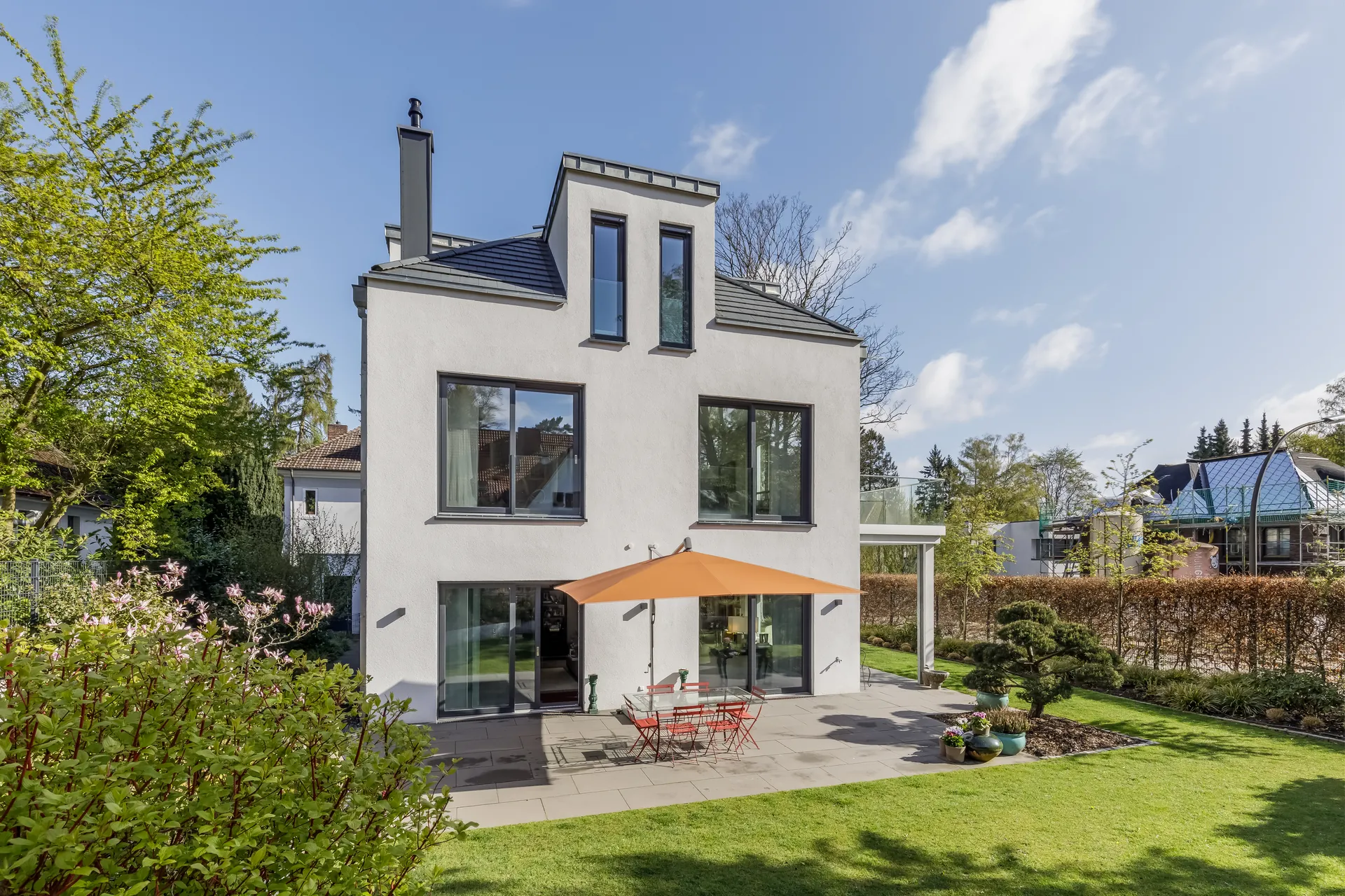 Weißes Einfamilienhaus mit Garten und Sonnenschirm auf der Terrasse