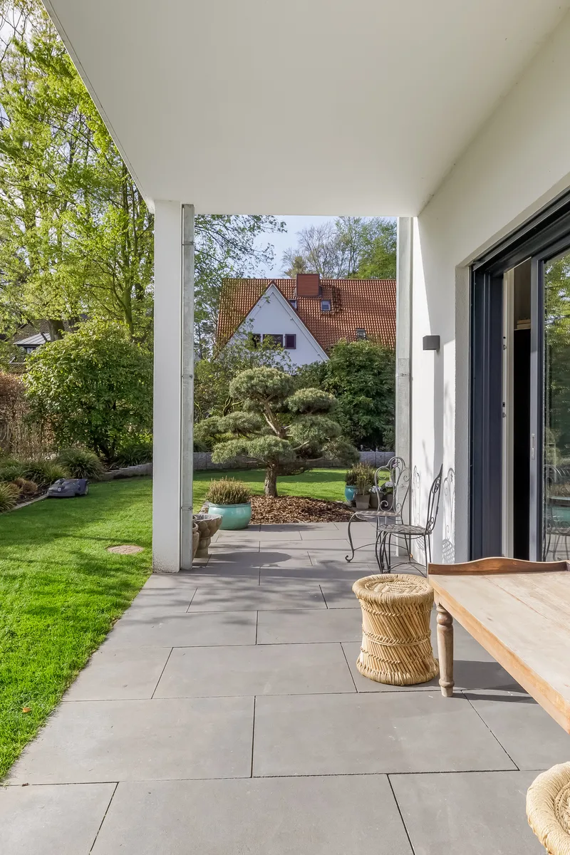 Überdachte Terrasse mit Holzbank vor großen Glastüren
