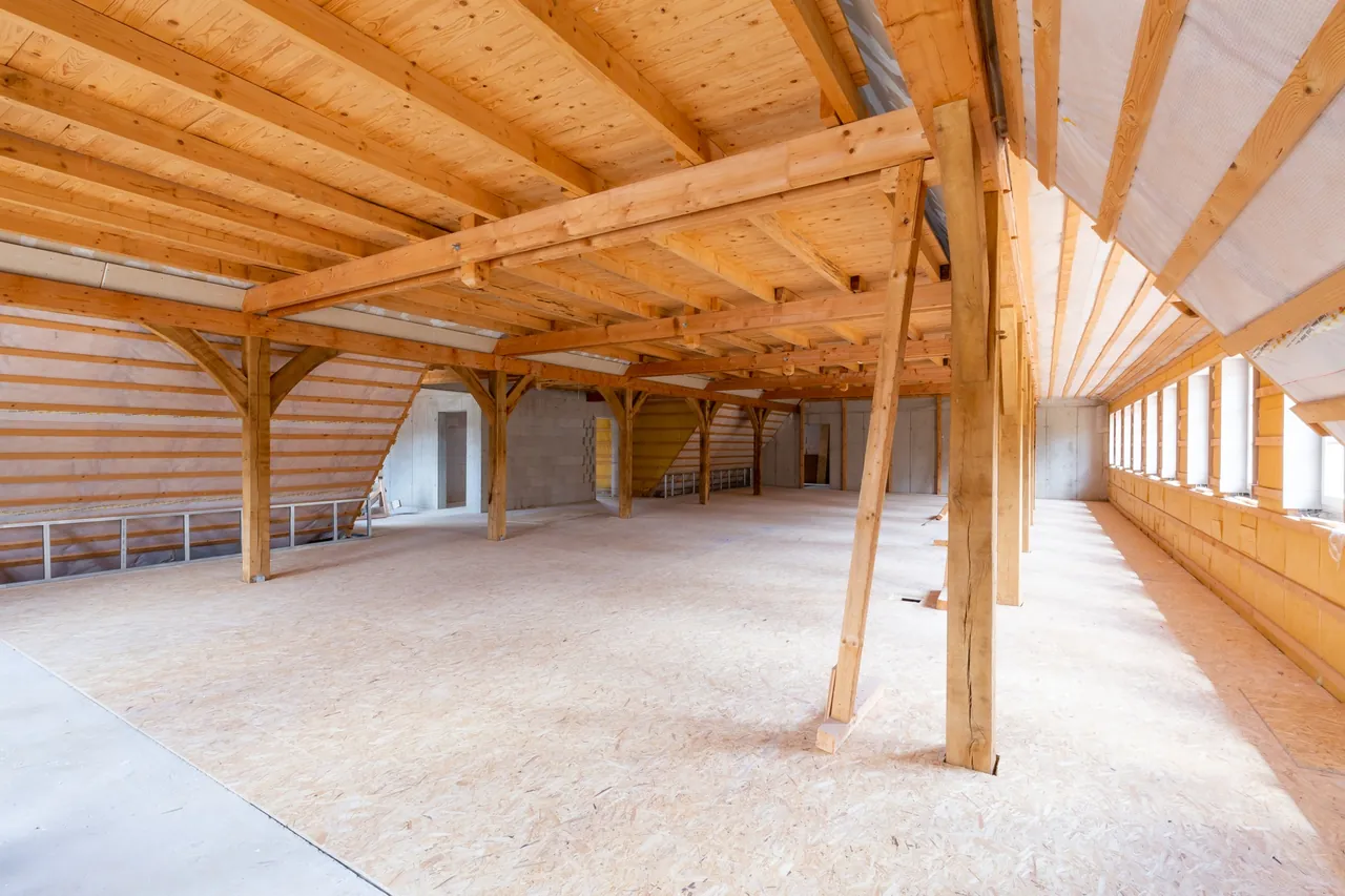 Rohbau: lang gestrecktes Dachgeschoss mit Holzstützen und Fensterreihe