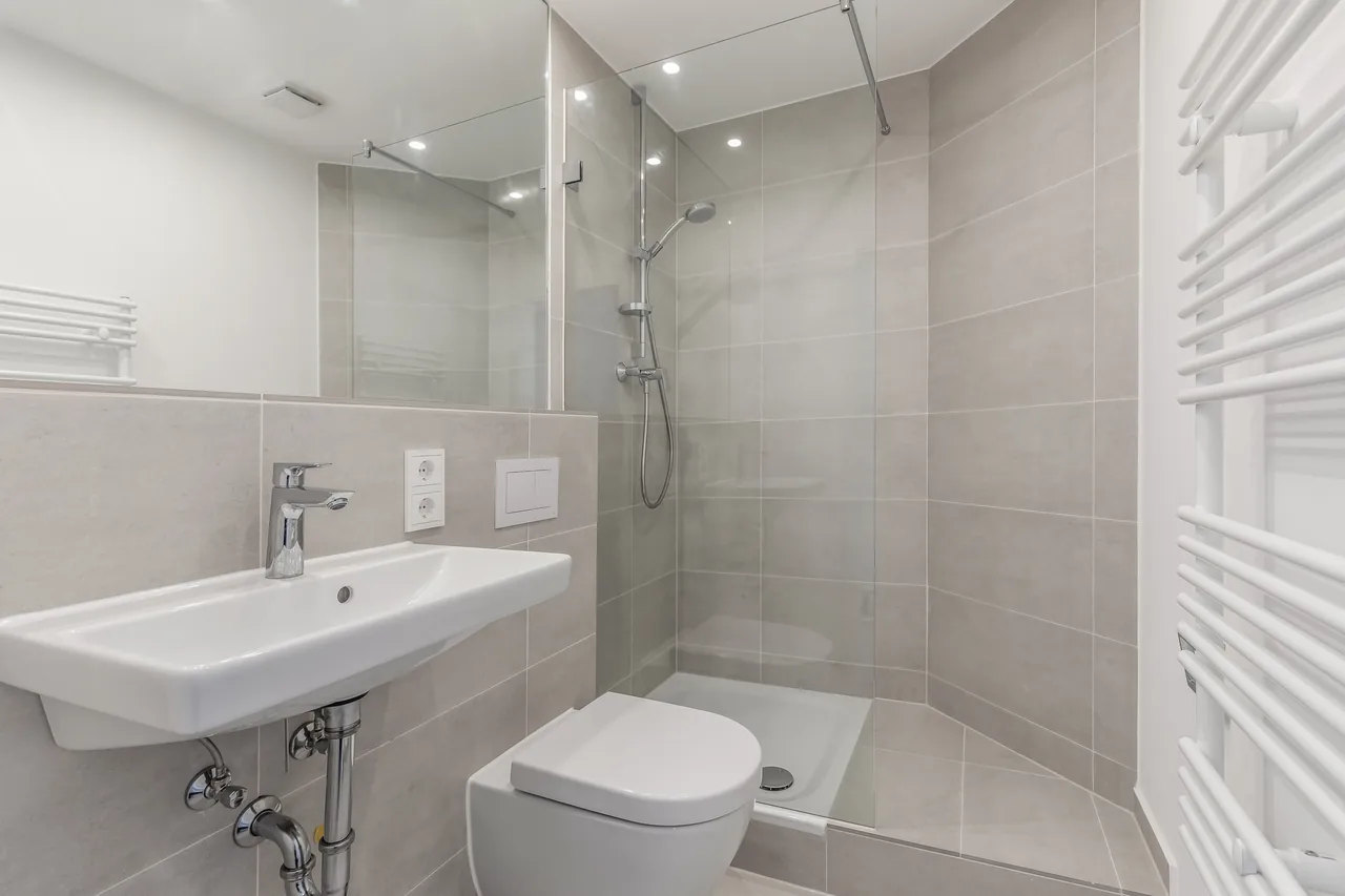 Nachher: dasselbe Bad mit großformatigen Fliesen, Dusche hinter Glas, Wand-WC und Handtuchheizkörper