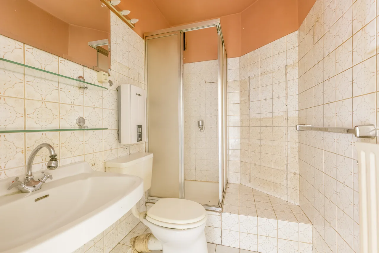 Vorher: Bad mit gemusterten Fliesen, Duschkabine, Waschbecken und Stand-WC
