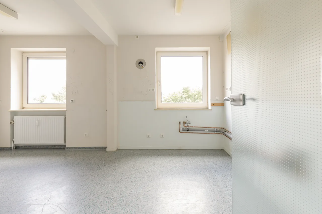 Vorher: ehemaliger Büroraum mit Linoleumboden, zwei Fenstern und offenen Leitungen an der Wand