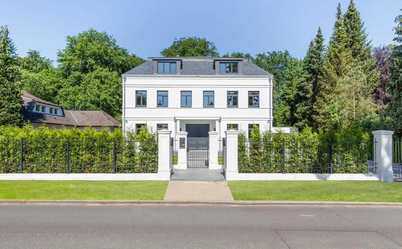Weiße Villa hinter einer Hecke, von der Straße aus fotografiert